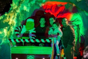 Family smiling, sitting in a sley next to the Grinch