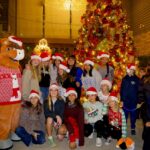 Friends and Family taking a picture with Sammy Clarita in front of the tree