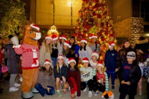 Friends and Family taking a picture with Sammy Clarita in front of the tree