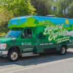Photo of the Library Express Bus wrapped with the Library Express logo and rolling green hills