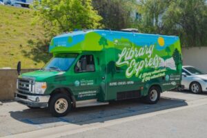 Photo of the Library Express Bus wrapped with the Library Express logo and rolling green hills