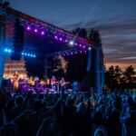 Dusk photo of concert, with blue and pink lights lighting up the cheering crowd