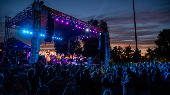 Dusk photo of concert, with blue and pink lights lighting up the cheering crowd
