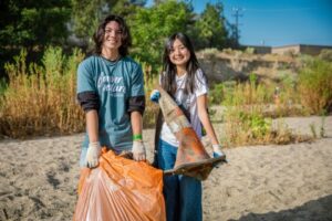 Volunteers smiling showing a full bag of trash and a traffic cone collected from the riverbed