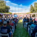 Crowd sitting at Veterans Historical Plaza in front of the flags