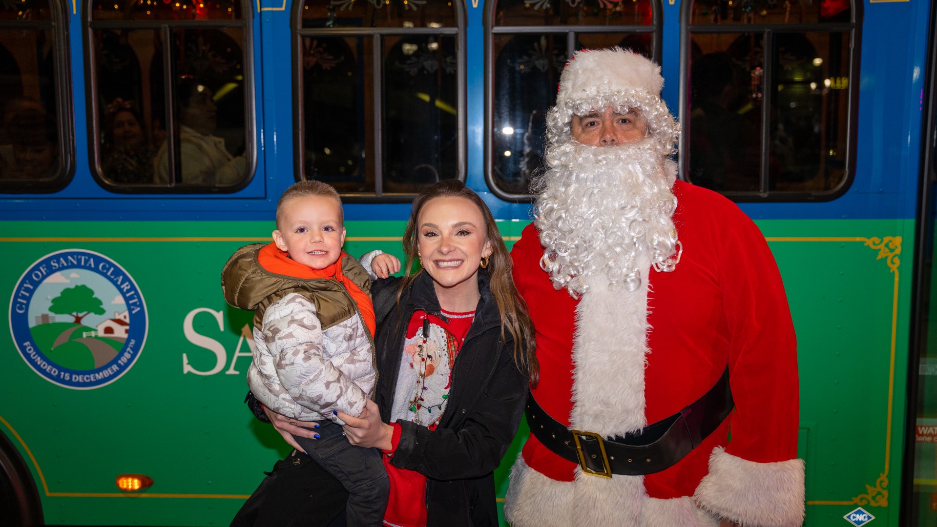 Santa and a mother and child in front of a Santa Clarita Transit Bus during the Holiday Light Tour.