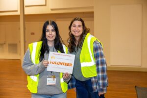 Two Volunteers wearing yellow vests holding a sign for the 2026 Greater Los Angeles Homeless Count.