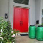 two green rain barrels in front of a home with two red doors.