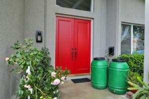 two green rain barrels in front of a home with two red doors.