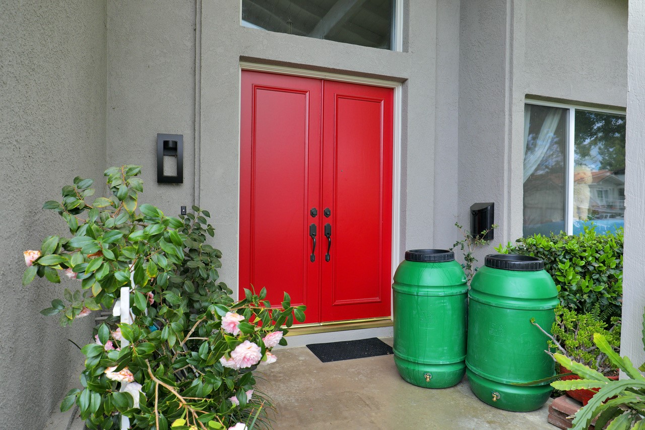 two green rain barrels in front of a home with two red doors.