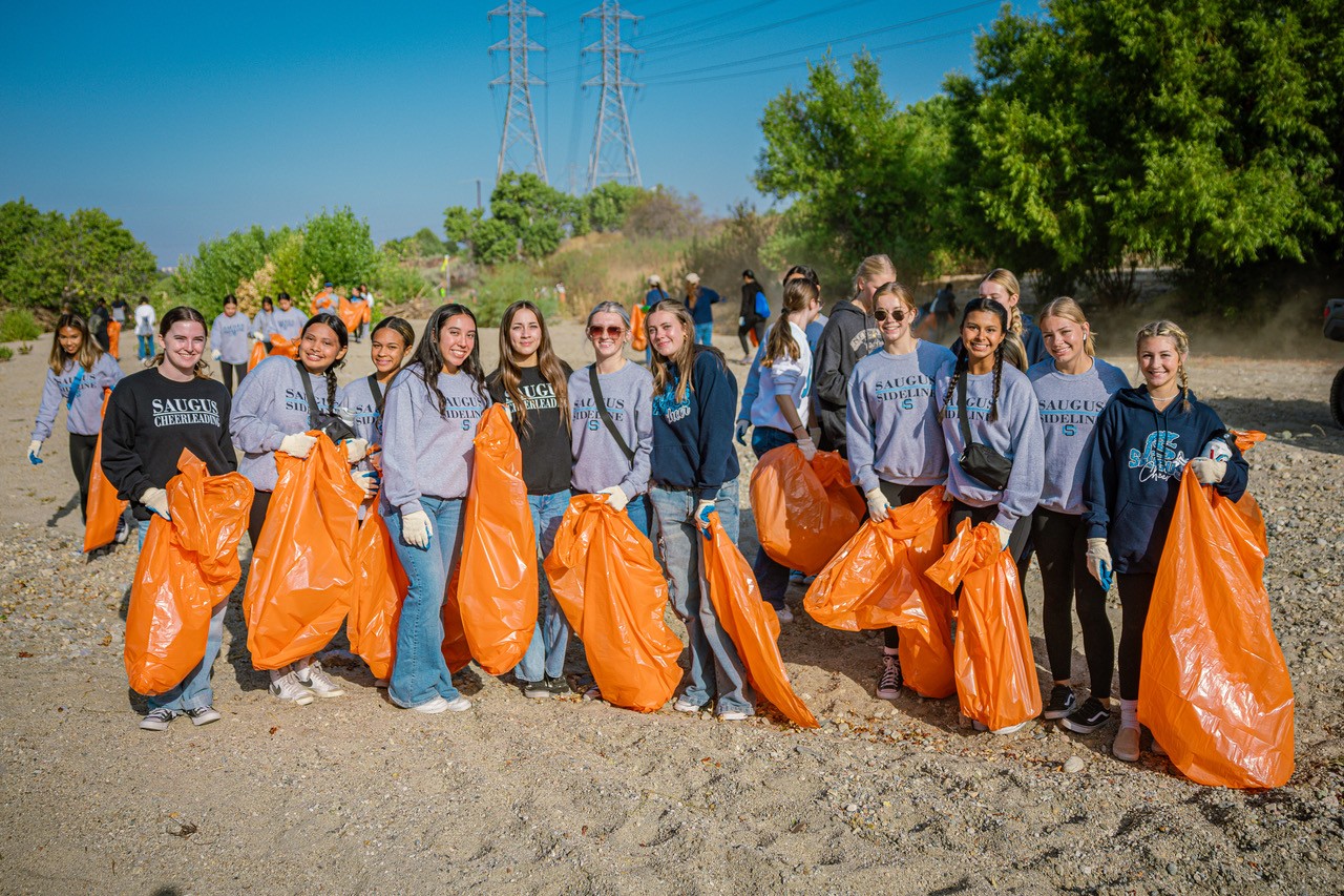 Members of the Saugus Cheer team stand in the Santa Clara riverbed holding orange bags to pick up trash during the annual River Rally.